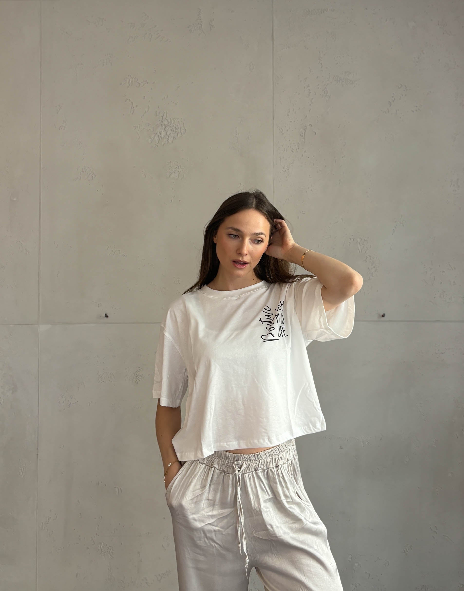 Frau mit braunen Haaren trägt weißes T-Shirt mit Aufschrift: positive vibes, mind, life