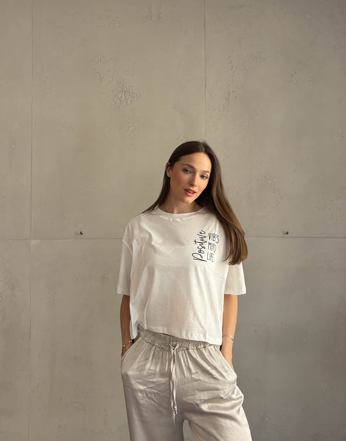 Frau mit braunen Haaren trägt weißes T-Shirt mit Aufschrift: positive vibes, mind, life