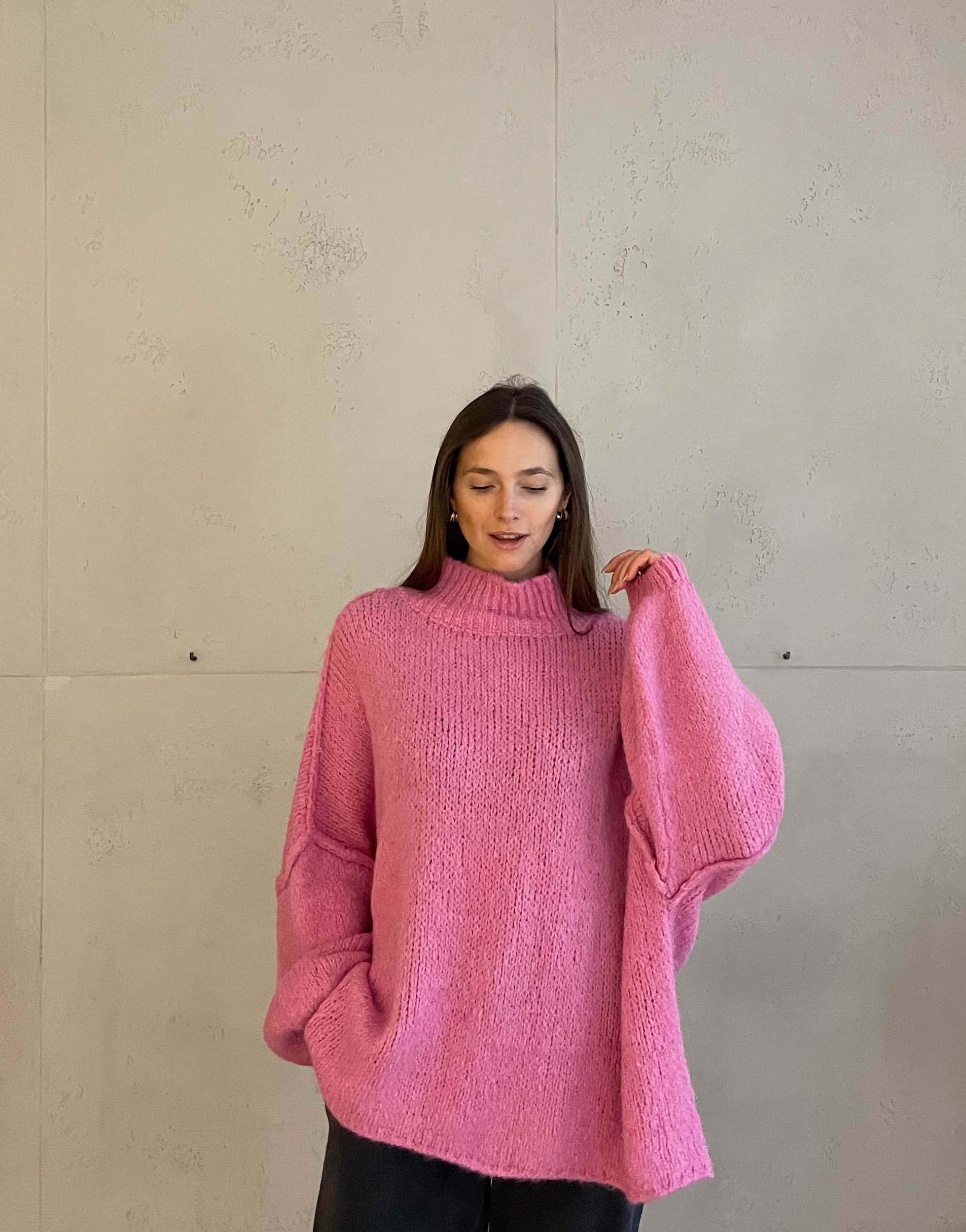 Frau mit brauen Haaren trägt oversize Pullover mit Stehkragen in pink