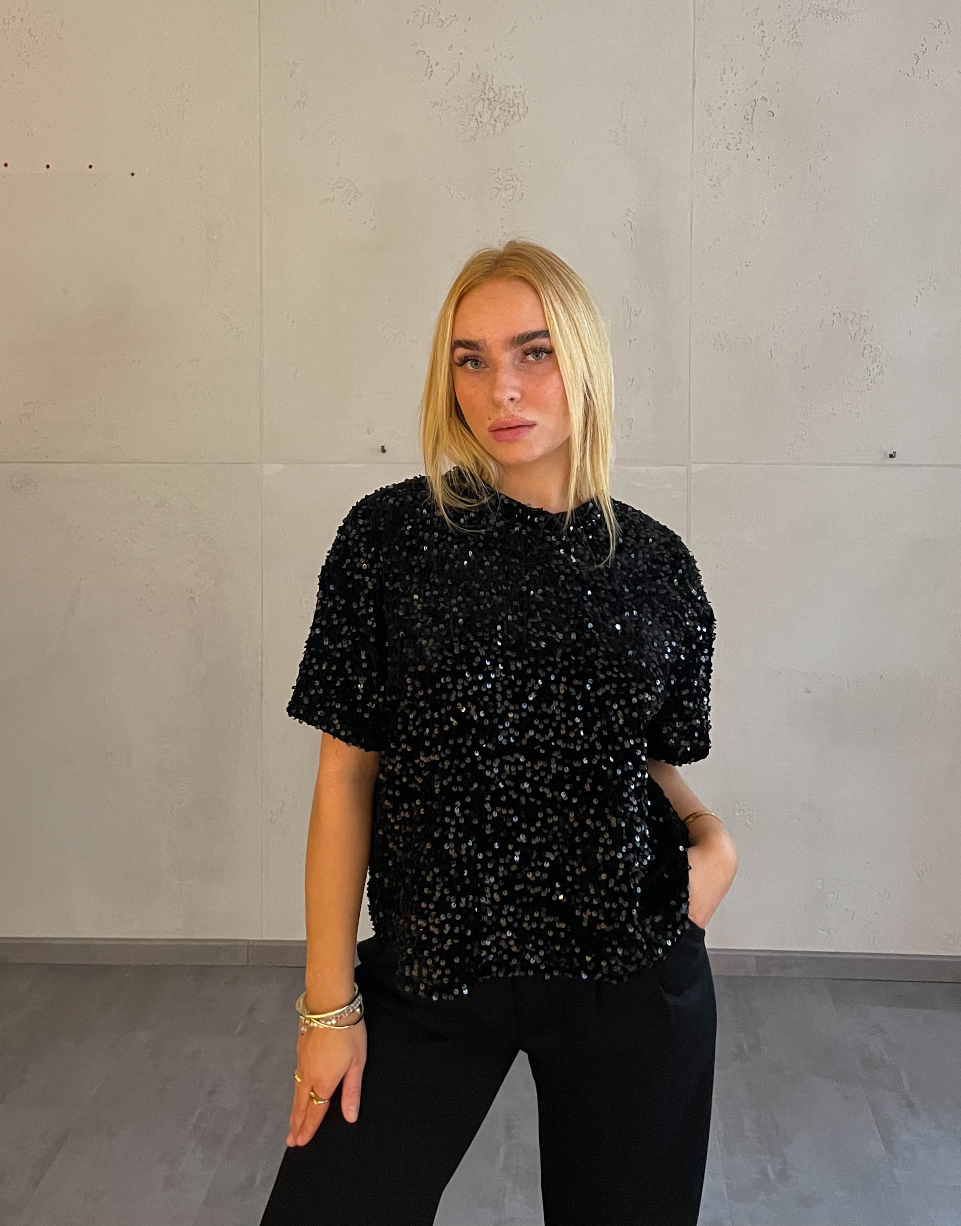Frau mit blonden Haaren trägt Samt Pailletten T-Shirt in Schwarz