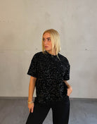 Frau mit blonden Haaren trägt Samt Pailletten T-Shirt in Schwarz