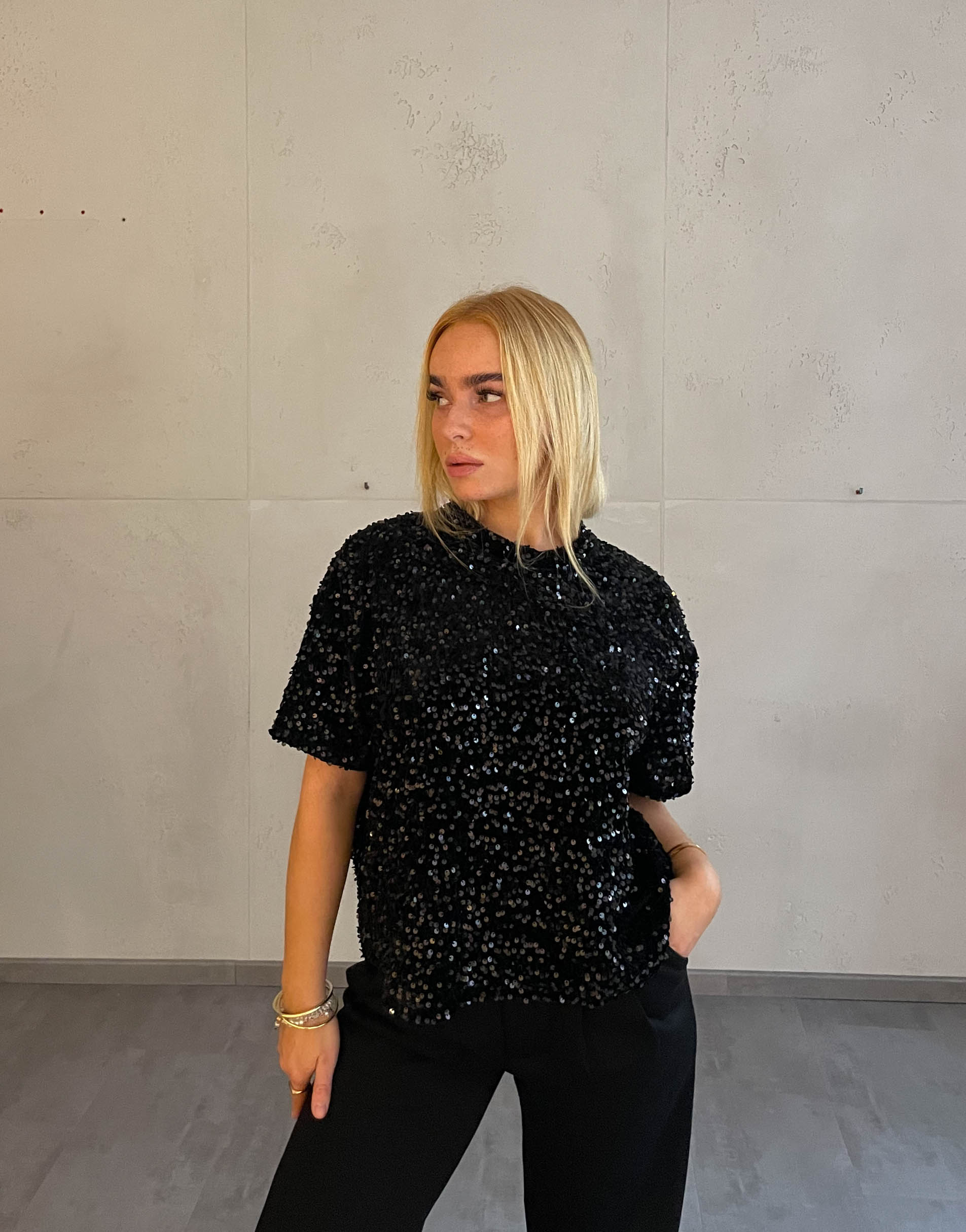 Frau mit blonden Haaren trägt Samt Pailletten T-Shirt in Schwarz