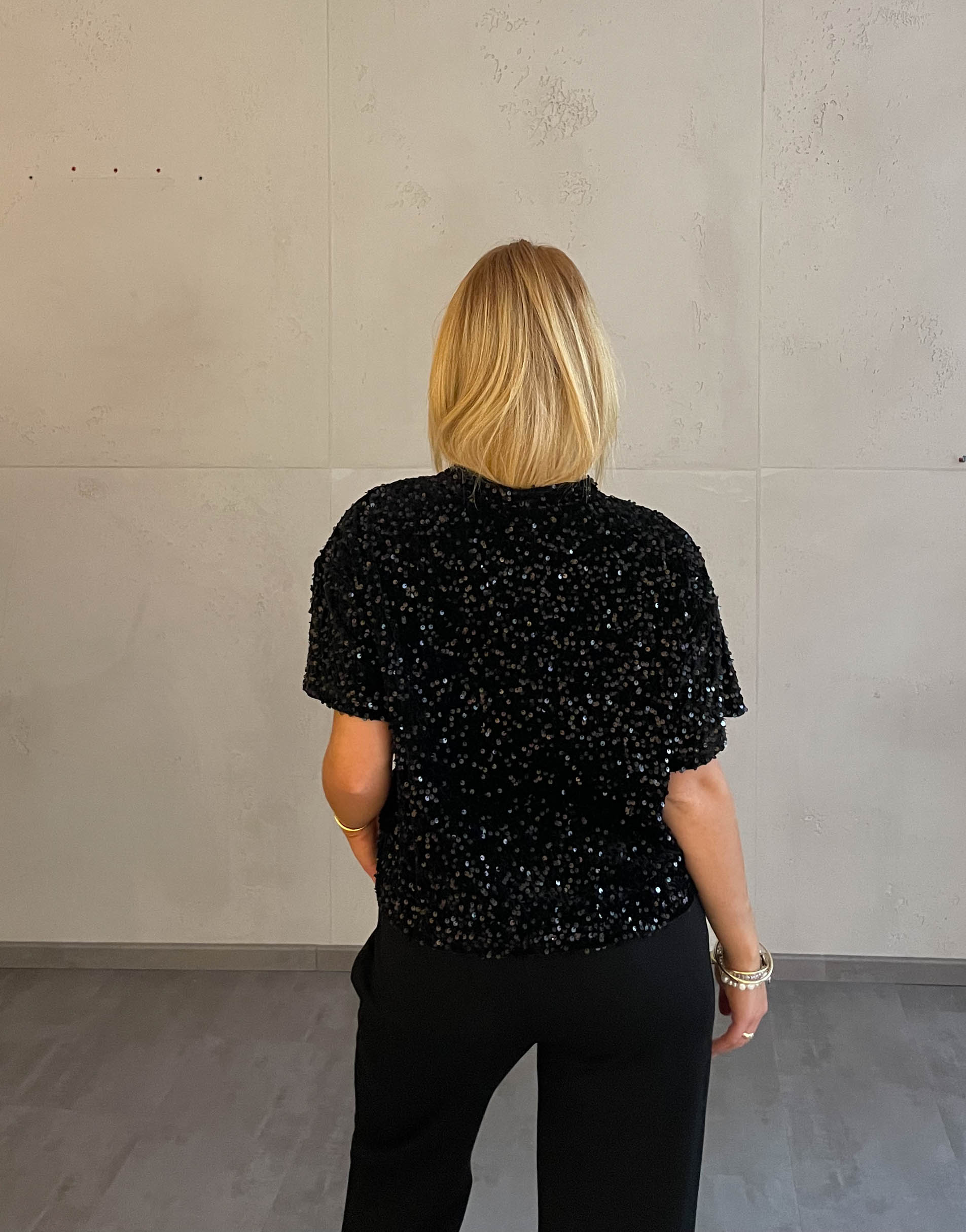 Frau mit blonden Haaren trägt Samt Pailletten T-Shirt in Schwarz