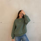 Frau mit brauen Haaren trägt Pullover mit Herz in grün