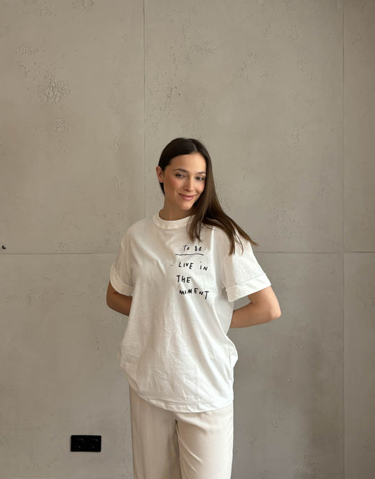 Frau mit brauen Haaren trägt weißes T-Shirt mit Schriftzug