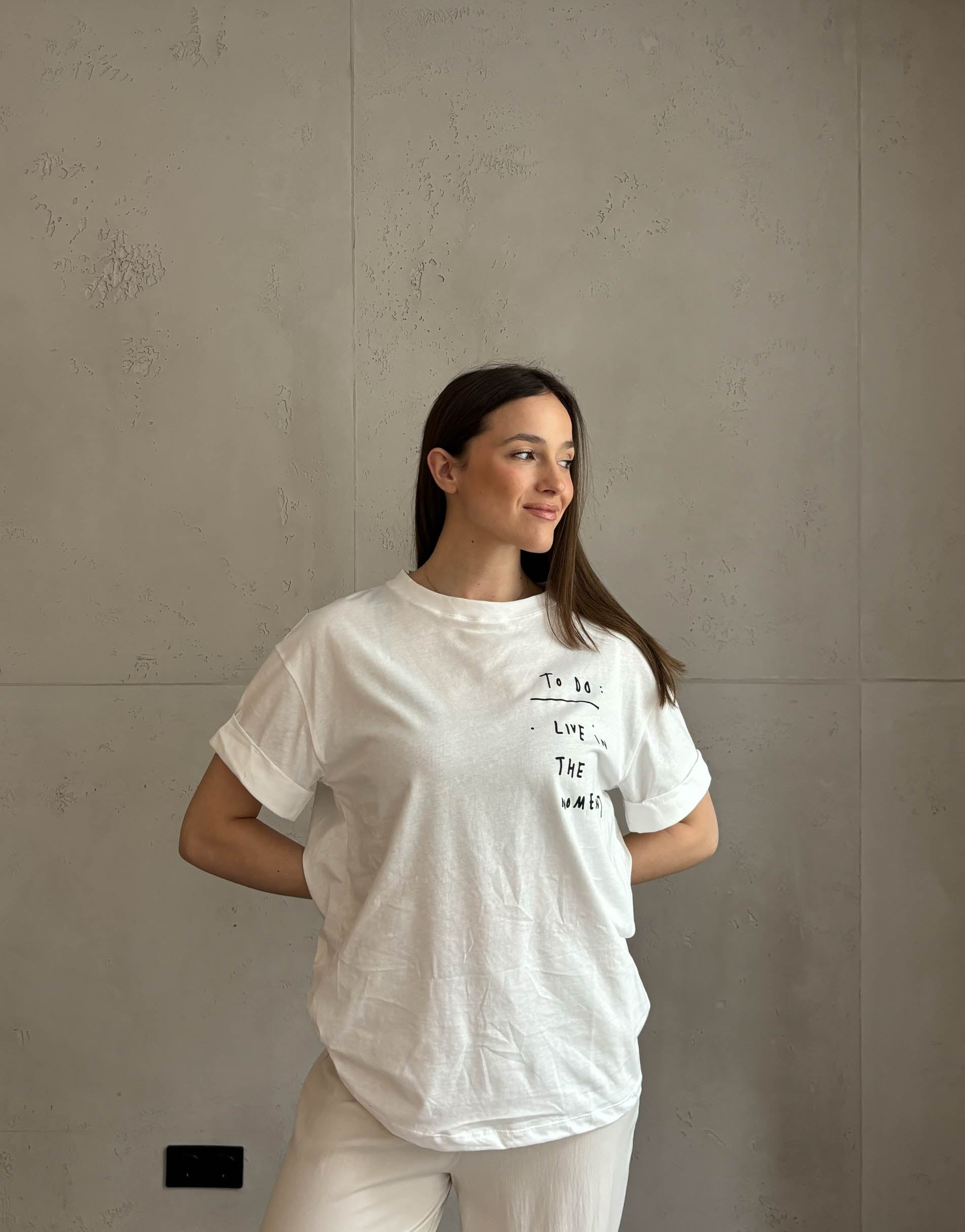 Frau mit brauen Haaren trägt weißes T-Shirt mit Schriftzug