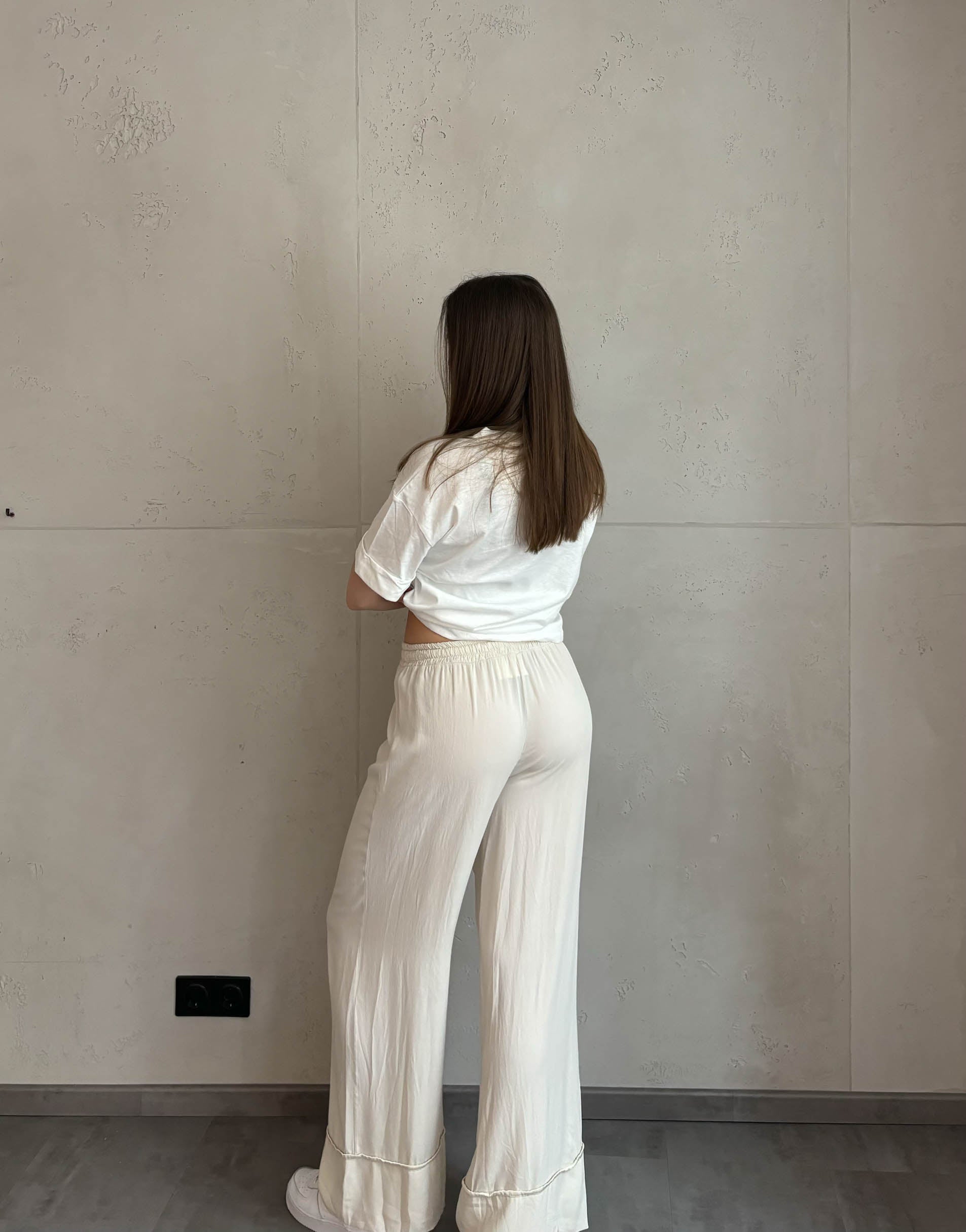 Frau mit brauen Haaren trägt Hose mit weitem Bein in Kombination mit weißem T-Shirt