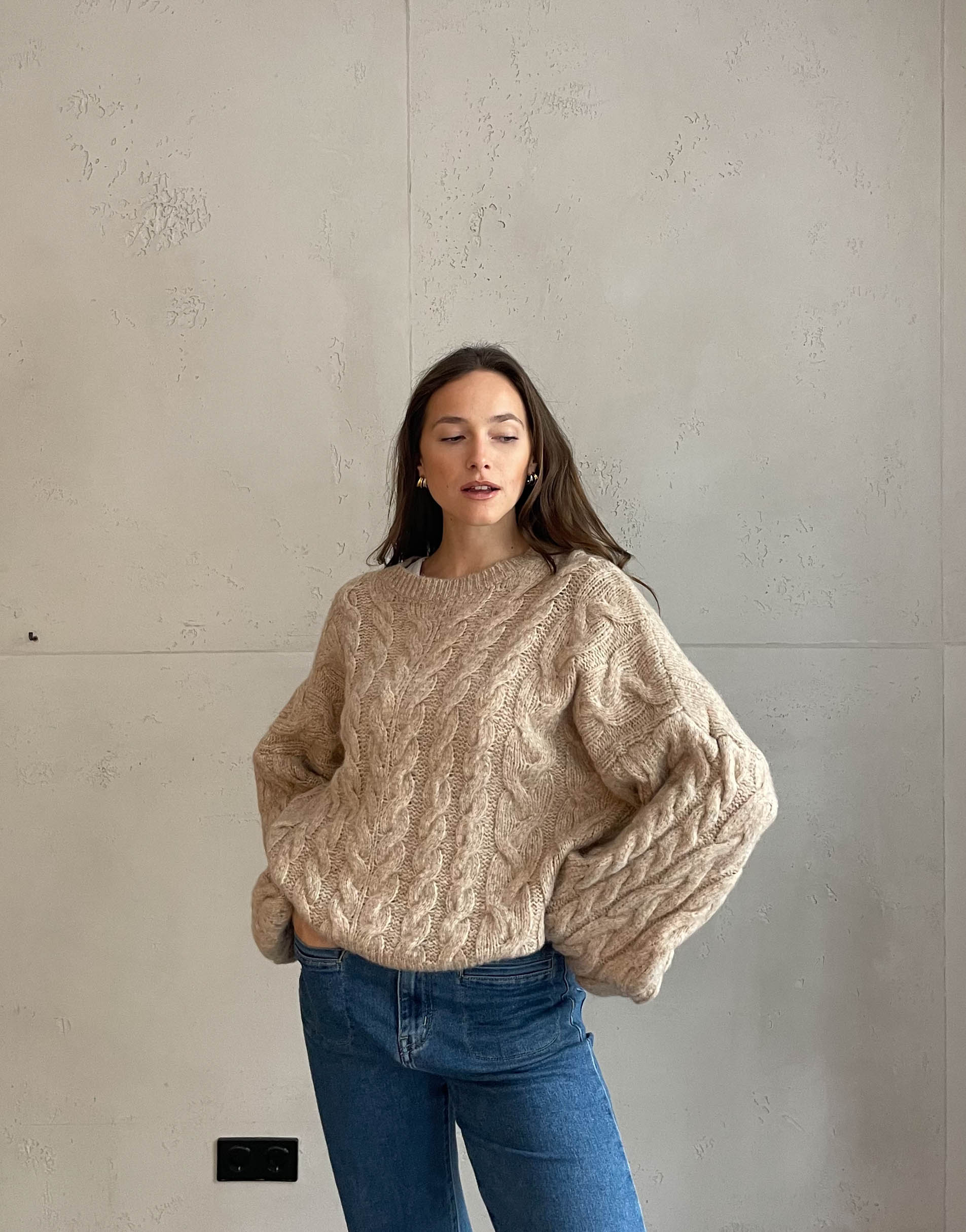 Frau mit brauen Haaren trägt Pullover mit Zopfmuster in beige