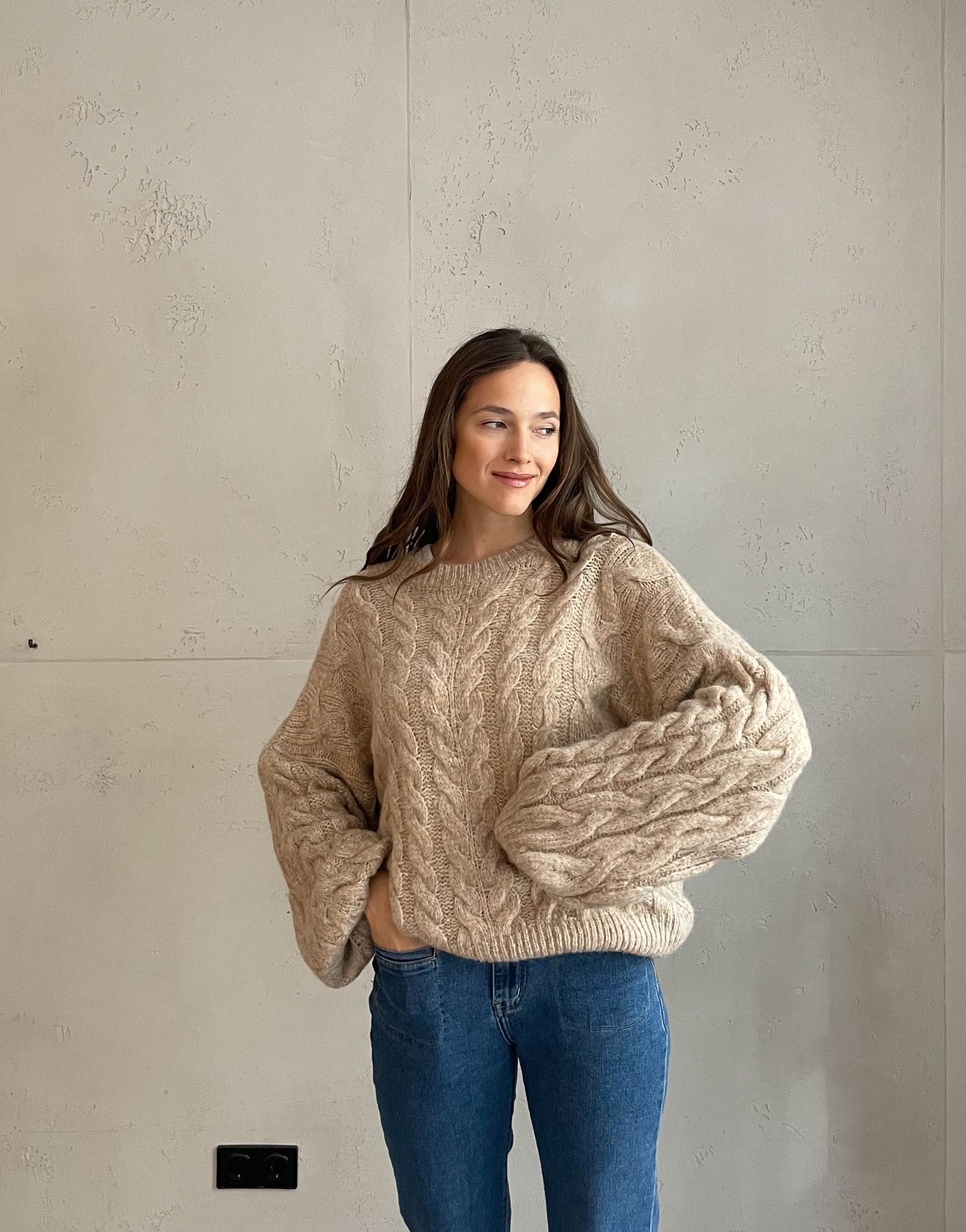 Frau mit brauen Haaren trägt Pullover mit Zopfmuster in beige