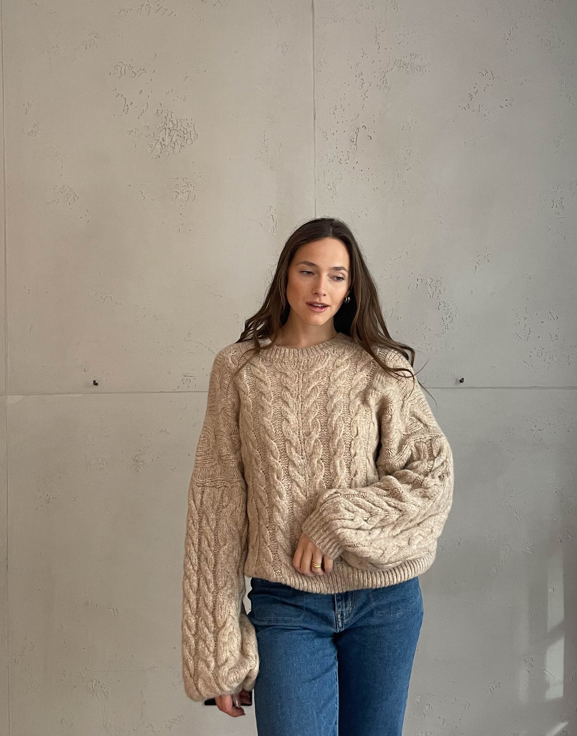 Frau mit brauen Haaren trägt Pullover mit Zopfmuster in beige