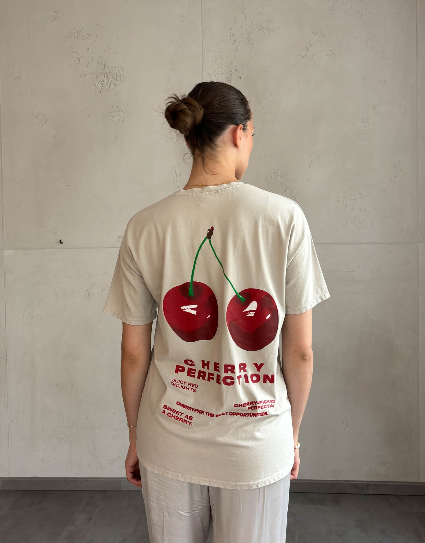 Frau mit brauen Haaren trägt beiges T-Shirt mit Cherry Print 