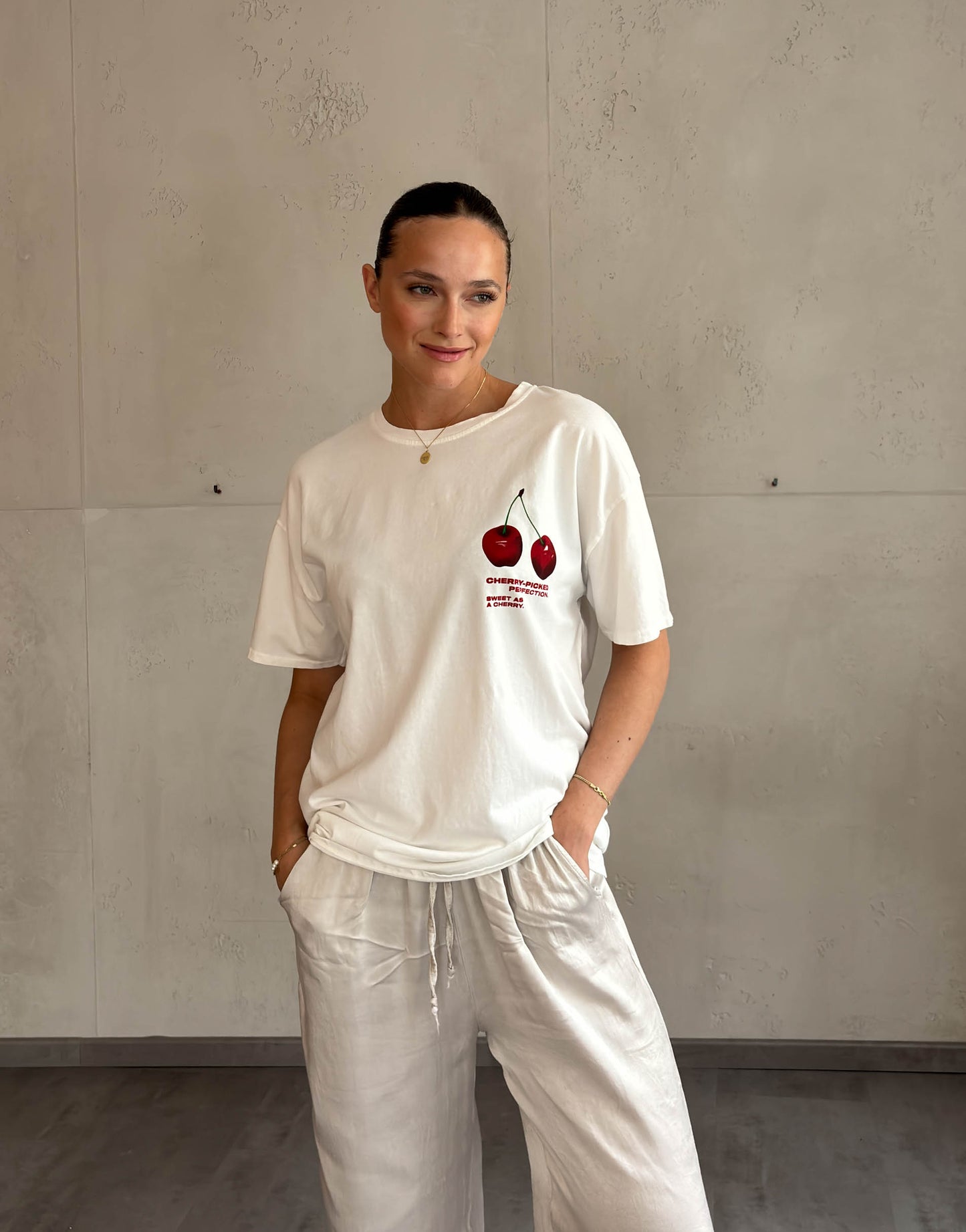 Frau mit brauen Haaren trägt weißes T-Shirt mit Cherry Print 