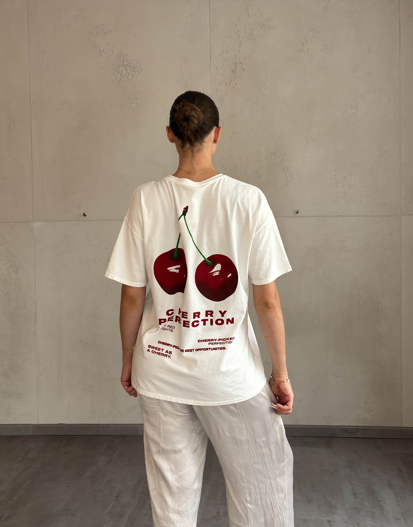 Frau mit brauen Haaren trägt weißes T-Shirt mit Cherry Print 