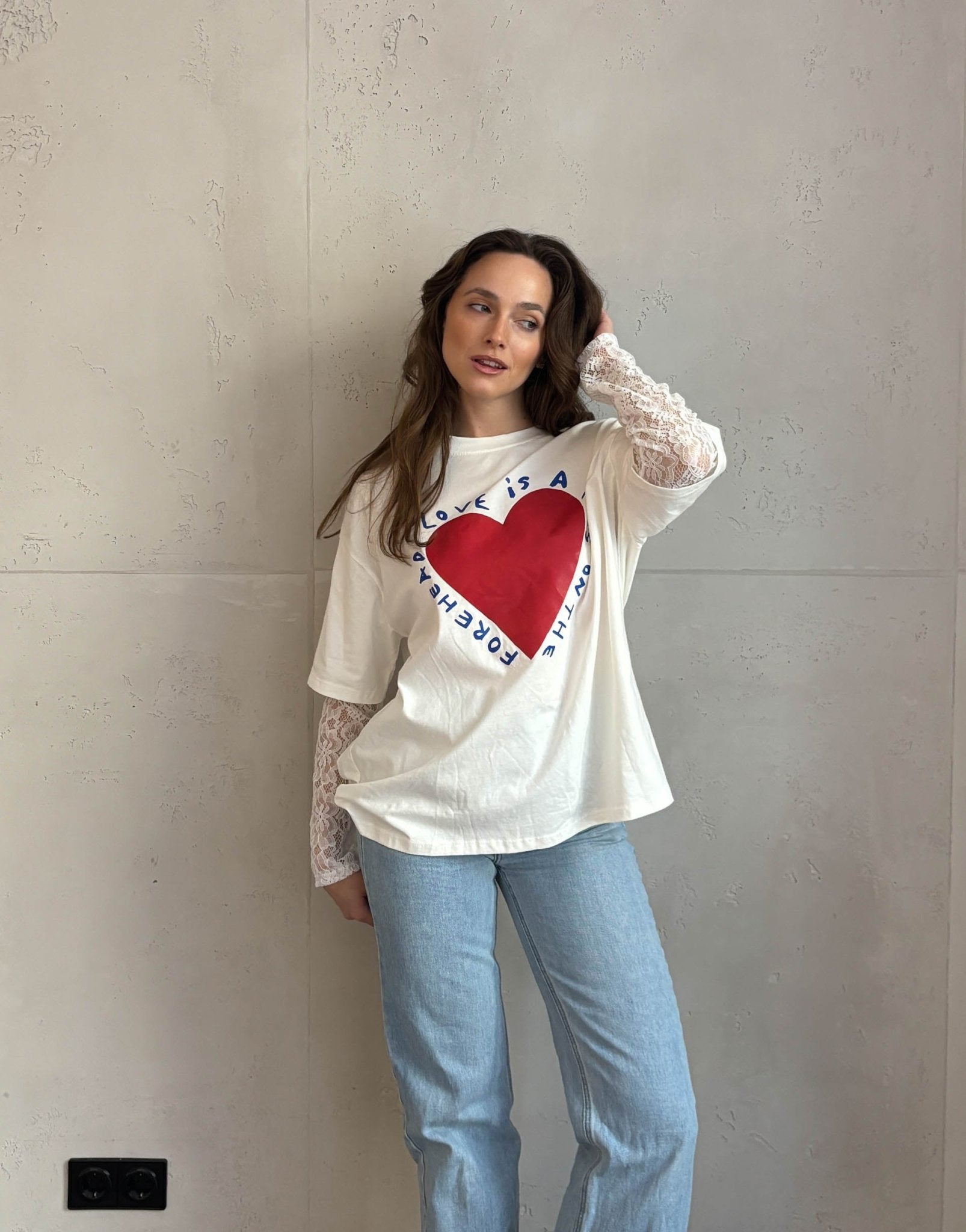 Frau mit braunen Haaren trägt weißes T-Shirt mit Print und Spitzeneinsatz am Arm