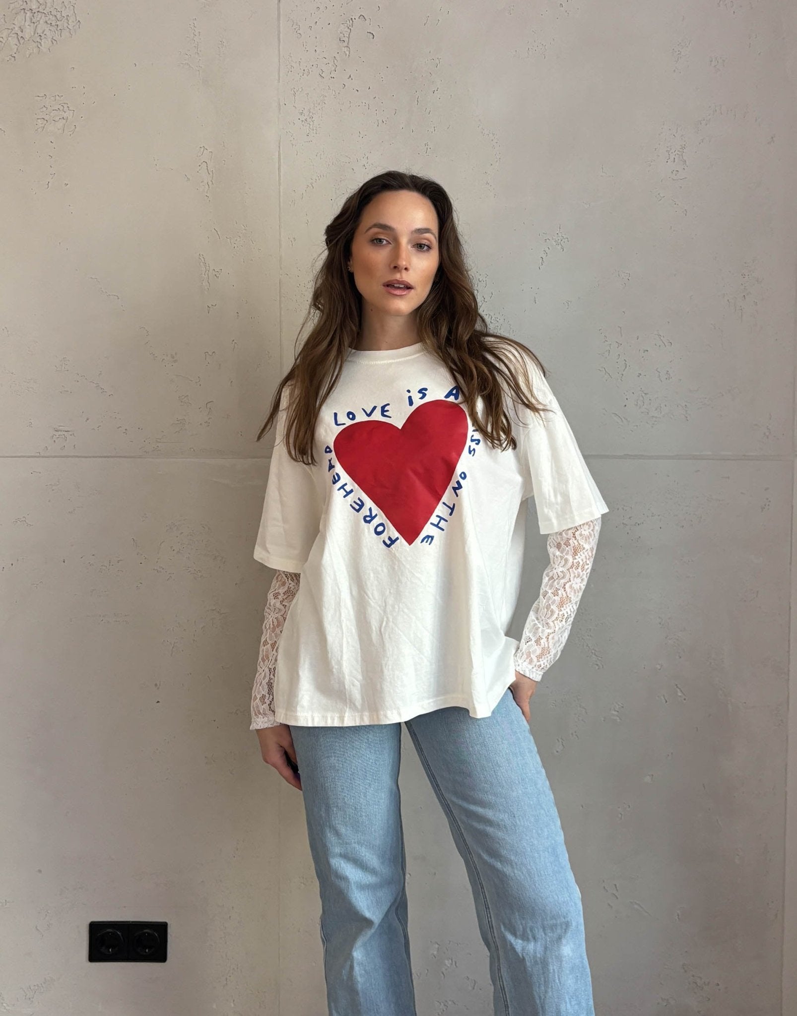 Frau mit braunen Haaren trägt weißes T-Shirt mit Print und Spitzeneinsatz am Arm