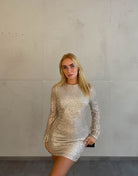 Frau mit blonden Haaren trägt kurzes Paillettenkleid in Gold