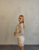 Frau mit blonden Haaren trägt kurzes Paillettenkleid in Gold