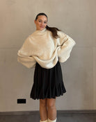 Frau mit braunen Haaren trägt kurzen oversize Pullover mit Stehkragen in hellbeige