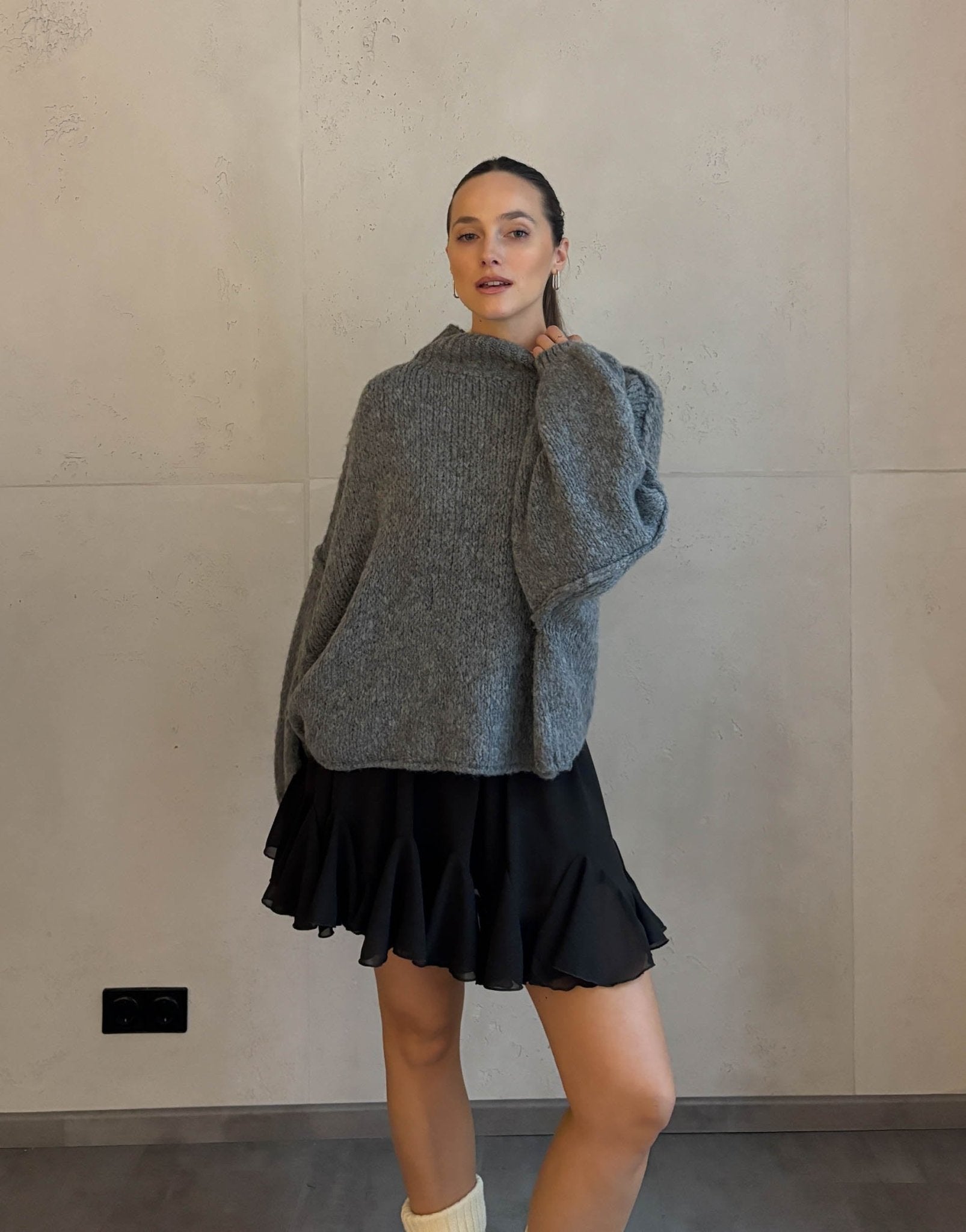 Frau mit braunen Haaren trägt kurzen oversize Pullover mit Stehkragen in dunkelgrau