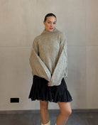 Frau mit braunen Haaren trägt kurzen oversize Pullover mit Stehkragen in taupe