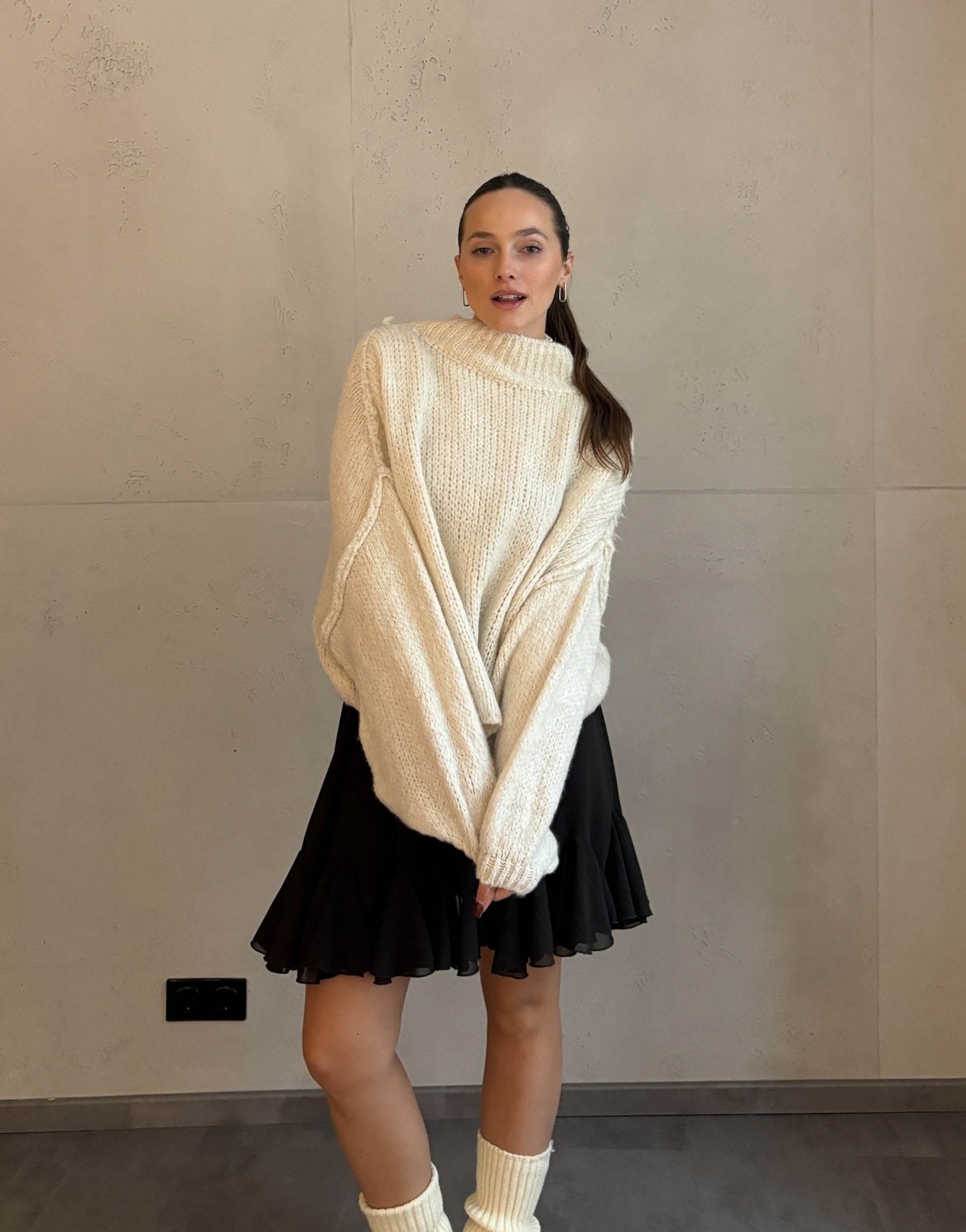 Frau mit braunen Haaren trägt kurzen oversize Pullover mit Stehkragen in hellbeige