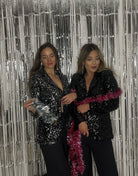Eine Frau ( links ) trägt einen Glitzerblazer mit silbernen Pailletten und die Frau daneben trägt einen Glitzerblazer in schwarz 