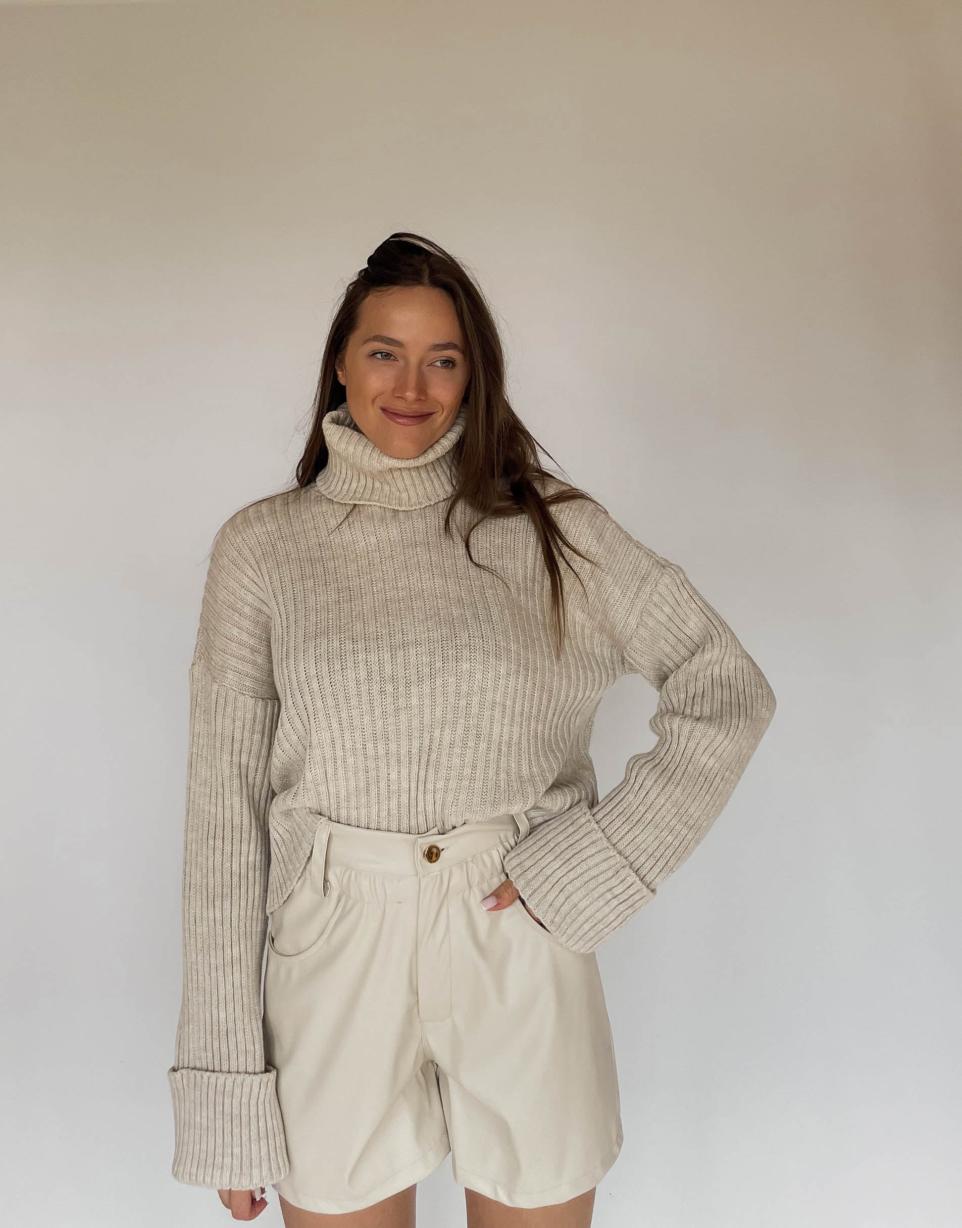 Frau mit brauen Haaren trägt Ledershorts in Beige mit Rollkragenpullover 