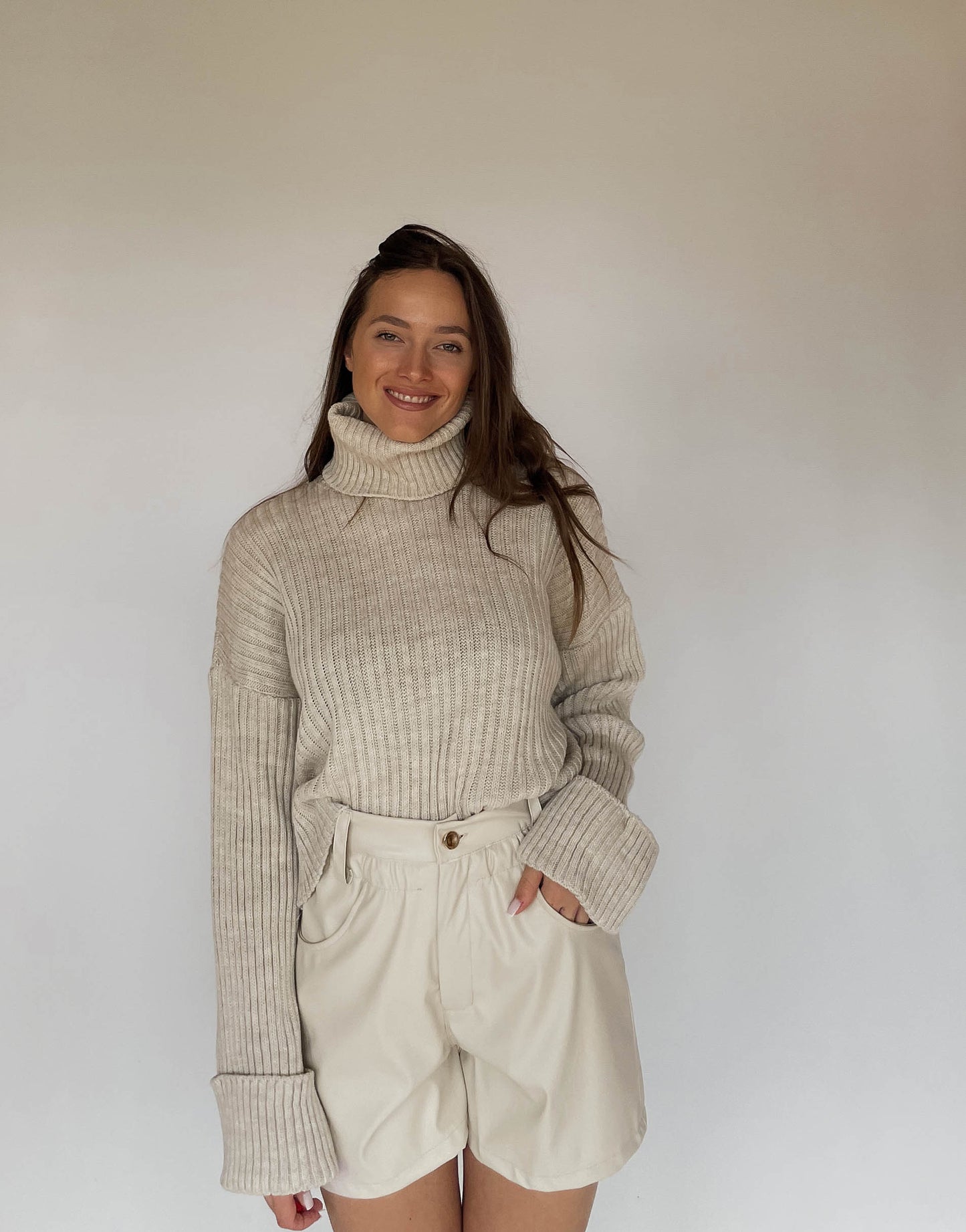 Frau mit brauen Haaren trägt Ledershorts in Beige mit Rollkragenpullover 